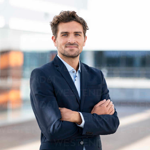 confident-businessman-standing-with-arms-crossed-against-building-SBOF02854